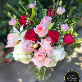 Arrangement of red and pink roses with white lilies and hydrangeas in a textured glass vase