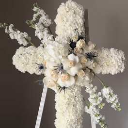 White floral cross on a stand with cream roses and dark accents