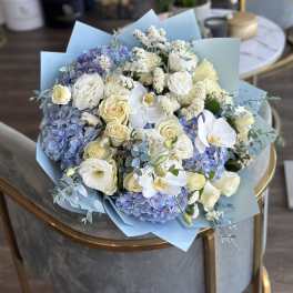 Bouquet of blue hydrangeas, white roses, and white orchids wrapped in pale blue paper