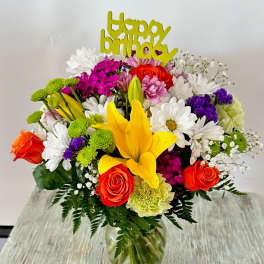 Colorful birthday bouquet in a glass vase with a yellow topper