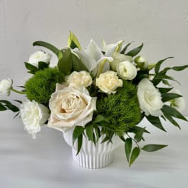 White roses and lilies arranged in a white vase with green filler
