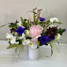 Mixed bouquet with pink peony, white orchids, and purple flowers in a white vase