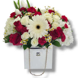 Red and white mixed flower arrangement with gerbera, roses, and tulips in a white box with chain handle