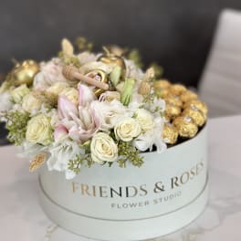 Round box of white and blush roses with gold chocolates on top