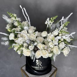 White roses and snapdragons arranged in a black hatbox.