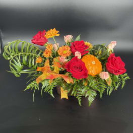 Autumn floral arrangement with red roses, orange daisies, and a small pumpkin in a low container