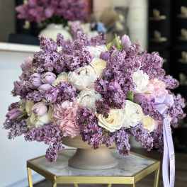 Lavender and white floral arrangement in a beige pedestal vase