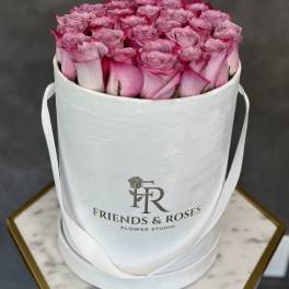 Pink roses arranged in a white round hat box with ribbon handles