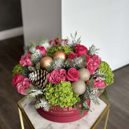 Pink roses and green hydrangeas in a round box with pinecones and ornaments