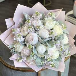 Bouquet of pale peonies and small lavender flowers wrapped in pink paper