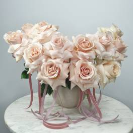 Blush pink roses arranged in a white vase with pink ribbons