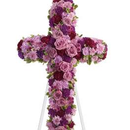 Cross-shaped floral tribute in pink, purple, and burgundy flowers on an easel