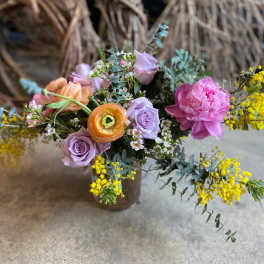 Mixed bouquet of pastel roses, peonies, and yellow filler flowers in a vase