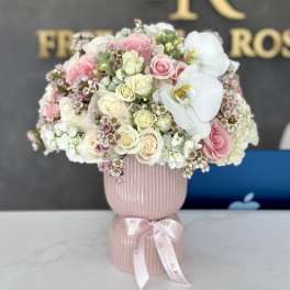 Pink and white rose arrangement in a ribbed pink vase with a ribbon