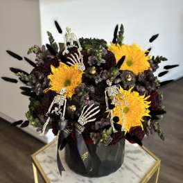 Black floral arrangement with yellow blooms and small skeleton decorations in a black vase