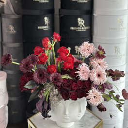 Mixed red, burgundy, and pale pink flowers in a white face vase