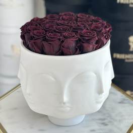 Deep burgundy roses arranged in a white sculptural face vase