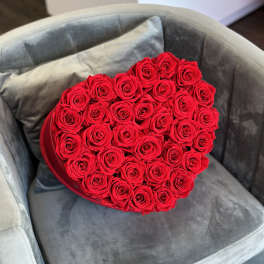 Heart-shaped box filled with red roses on a gray chair