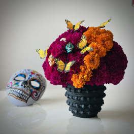 Marigold arrangement in a black vase with butterfly picks and a decorative skull beside it