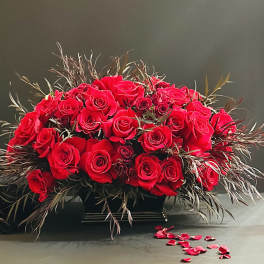 Large arrangement of red roses in a black container with scattered petals