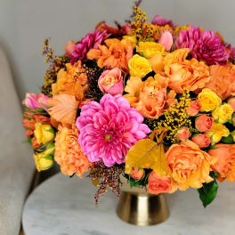 Bright mixed bouquet of orange, pink, and yellow flowers in a gold vase