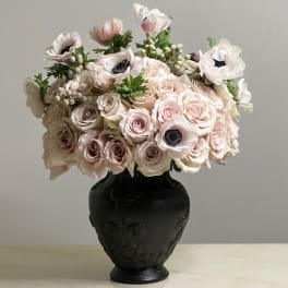 Blush roses and pale anemones arranged in a black vase