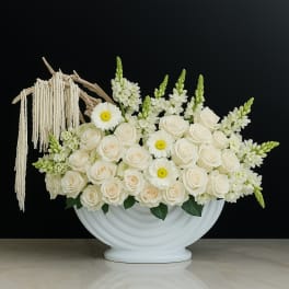 White roses and daisy-like flowers in a white vase with macramé tassels