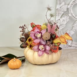 Floral arrangement in a pumpkin-shaped container with a small pumpkin beside it