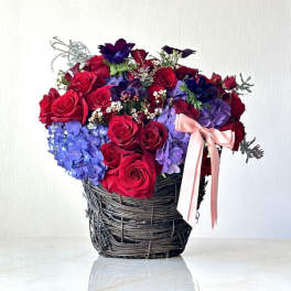 Bouquet of red roses and blue hydrangeas in a woven basket with a pink ribbon