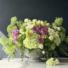 Lavender roses and pale green flowers in a gray pedestal vase