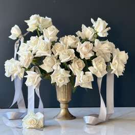 White roses arranged in a gold vase with long satin ribbons.