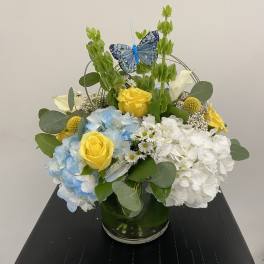 Blue and white hydrangeas with yellow roses in a glass vase