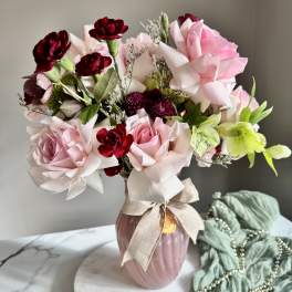 Pink and burgundy roses arranged in a vase with a ribbon bow