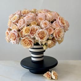 Peach and blush roses arranged in a striped vase on a black stand