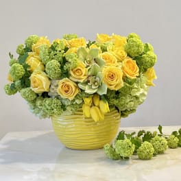 Yellow roses and green hydrangeas arranged in a yellow vase.