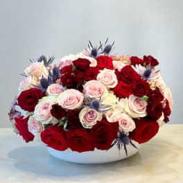 Red and blush roses arranged in a white bowl vase