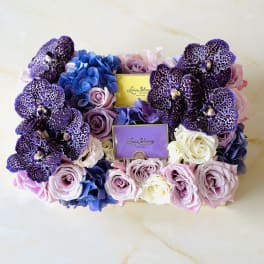 Box of purple orchids and pastel roses with two perfume boxes