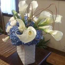 White calla lilies arranged with blue hydrangeas in a tall white vase