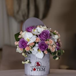 Bouquet of purple roses, white orchids, and peach spray roses in a gray box