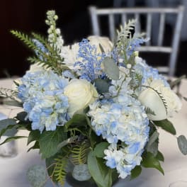 Blue hydrangeas and white roses arranged in a low centerpiece vase