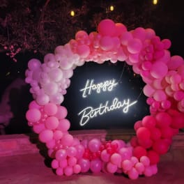 Pink balloon arch around a neon Happy Birthday sign