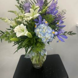 White lilies and blue-purple flowers in a glass vase