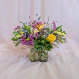 Bouquet of yellow roses and pink filler flowers in a square glass vase
