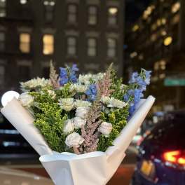 Bouquet of white and blue flowers wrapped in white paper with a yellow ribbon