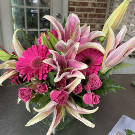 Pink lilies, gerbera daisies, and roses in a glass vase