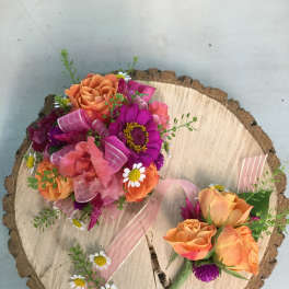 Two small rose bouquets with pink ribbon on a wood slice