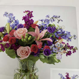 Mixed bouquet of pink, purple, and blue flowers in a clear glass vase