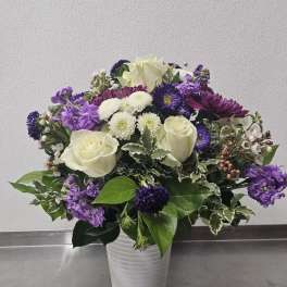 White roses and purple mixed flowers arranged in a white ceramic vase