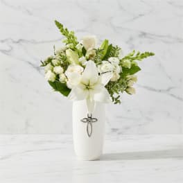 White lily and rose arrangement in a white vase with a cross charm