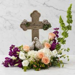Floral arrangement with peach and white roses around a decorative cross and bird figurines